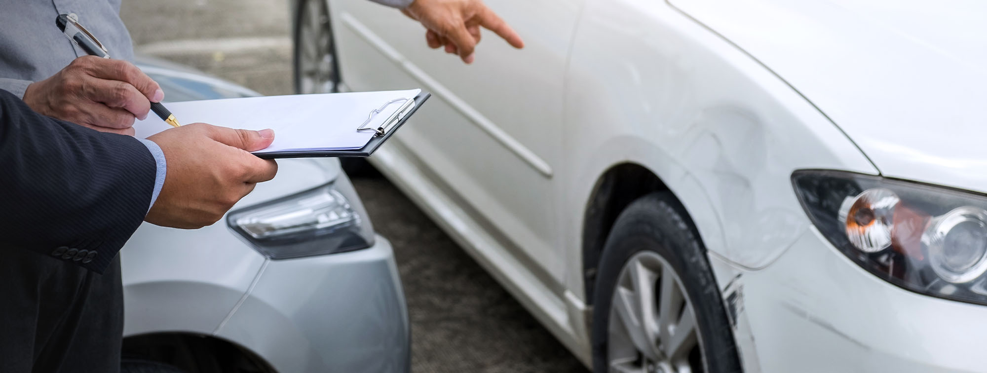 Person signing documents pointing at a damaged vehicle